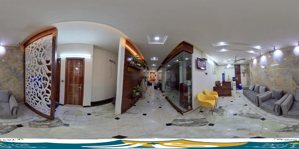 A wide-angle interior view of the clinic corridor, showing marble flooring, a carved wooden room divider, yellow upholstered chairs and glass-partitioned rooms leading off the hallway.