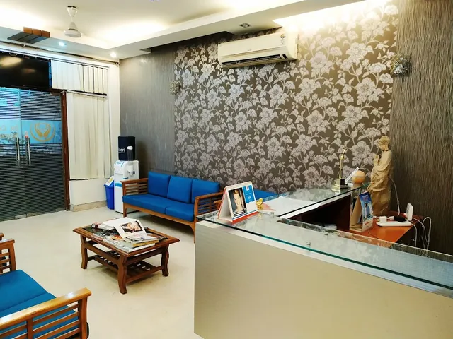The clinic waiting area: two blue upholstered wooden sofas and a low wooden table with magazines, facing a glass-fronted reception desk against a floral-patterned accent wall.